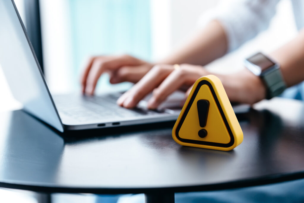 A person typing on a laptop with a caution sign on it.