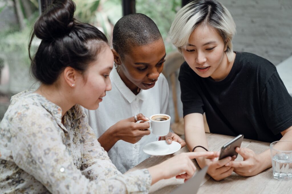 Three women sitting around a table looking at a smartphone.