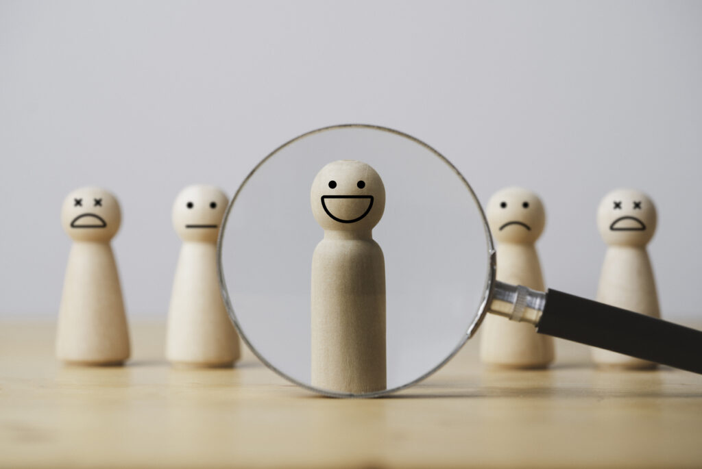 A group of wooden figures with a smiley face under a magnifying glass.