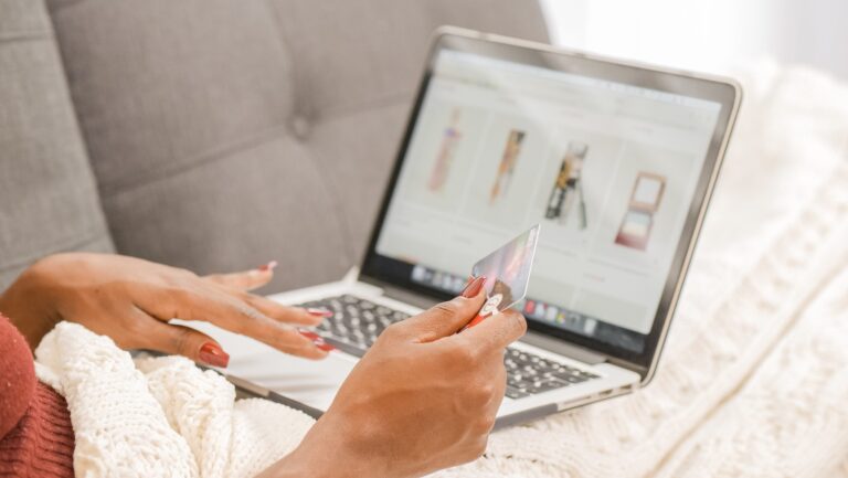 A woman engages in omnichannel marketing while sitting on a couch, utilizing a laptop and a credit card.